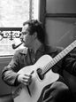 Photo Georges Brassens près de la fenêtre avec sa guitare, Paris, 1953 - 15 x 20