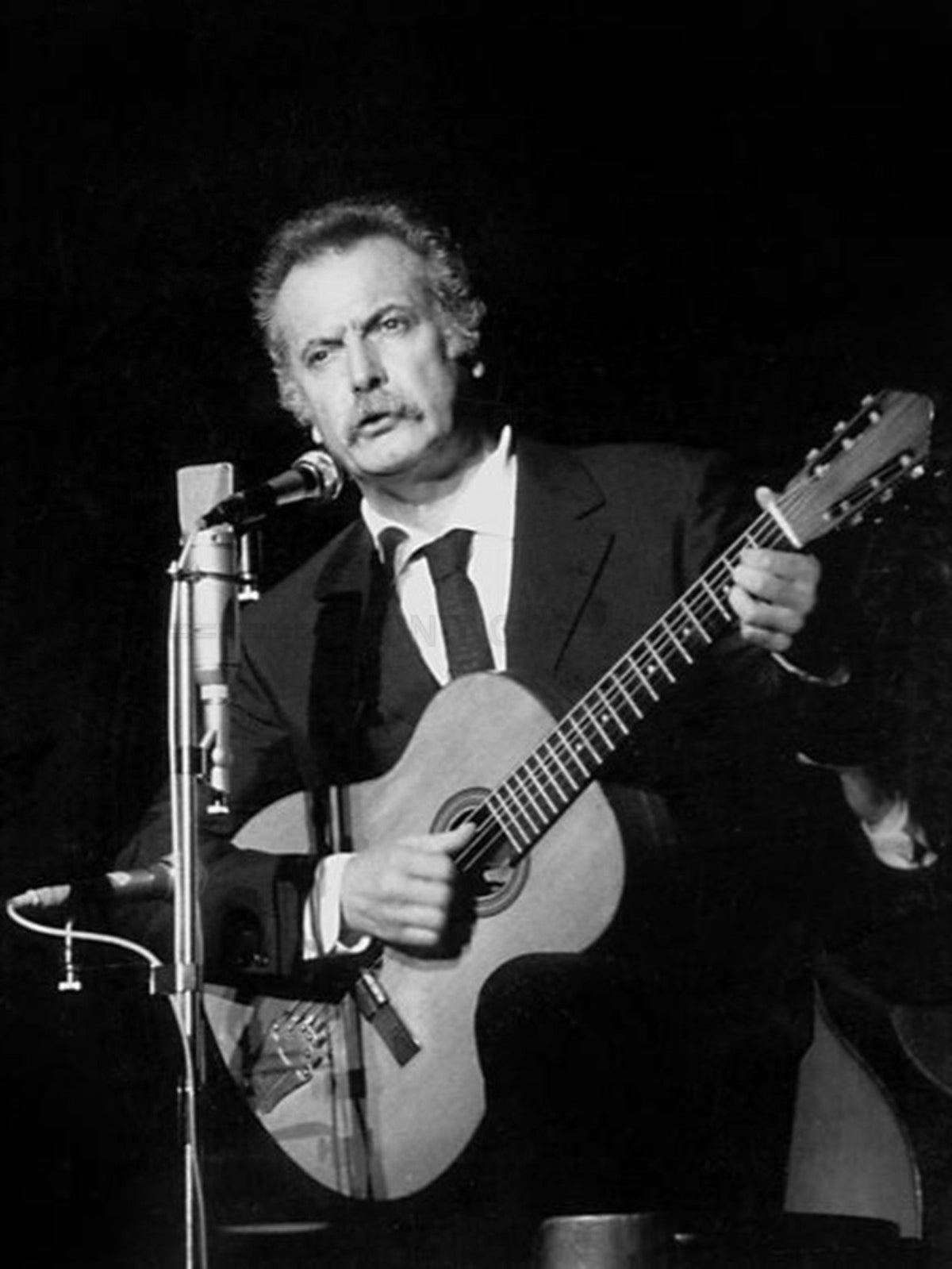 Photo Georges Brassens jouant de la guitare en chantant sur scène - 15 x 20