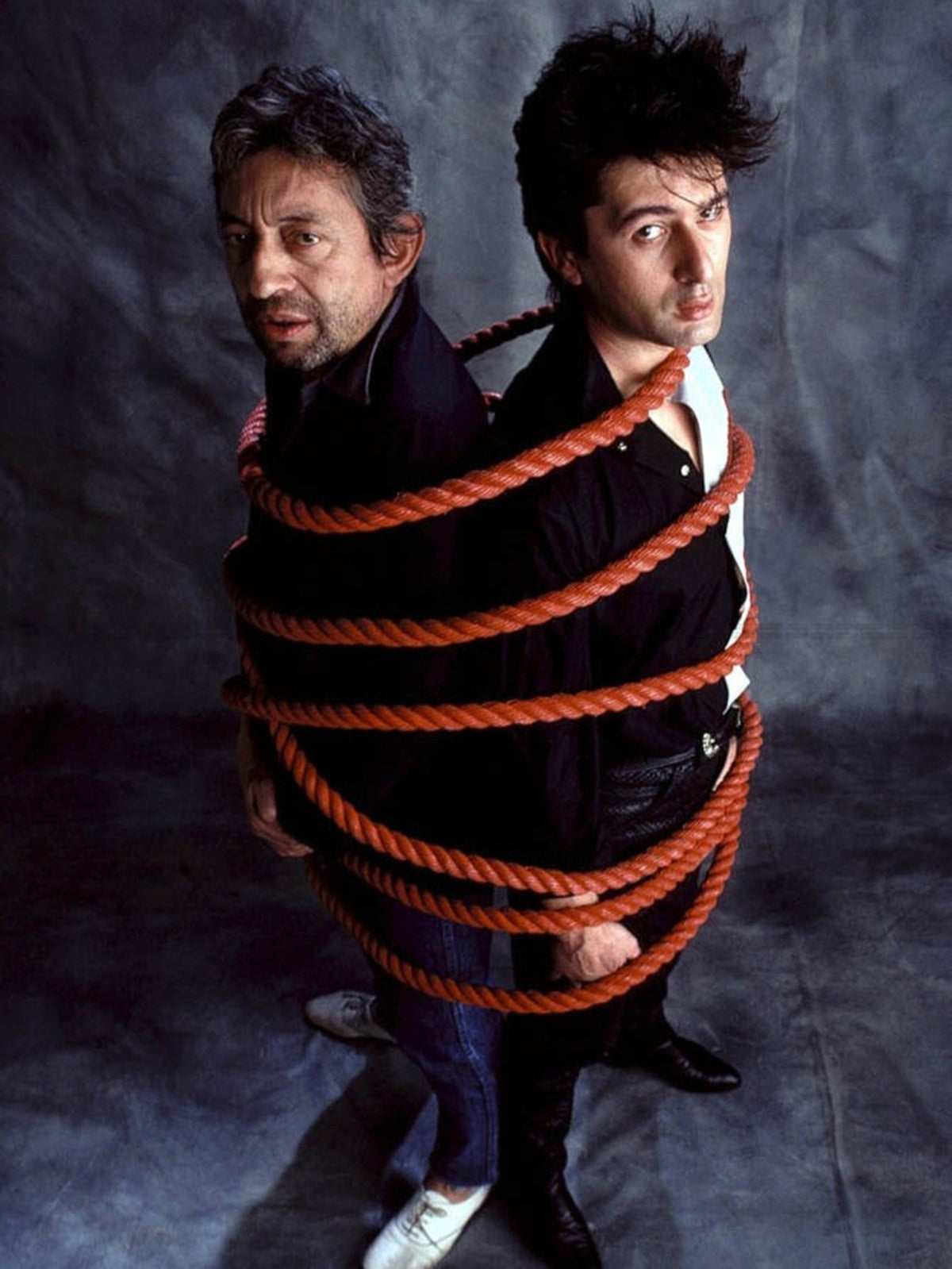 Photo Serge Gainsbourg & Alain Bashung dos à dos par une corde en 1982 - 15 x 20
