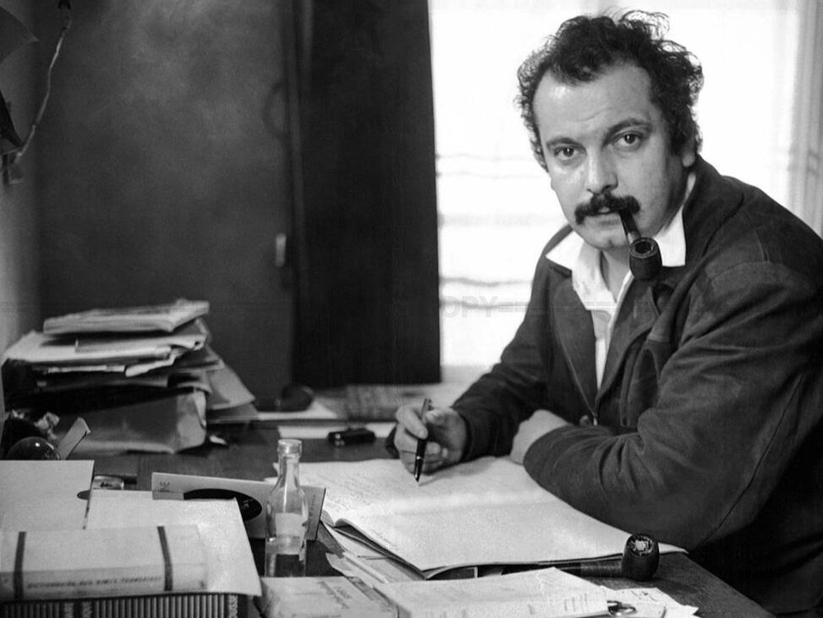 Photo Georges Brassens écrivant à son bureau, une pipe à la bouche - 15 x 20